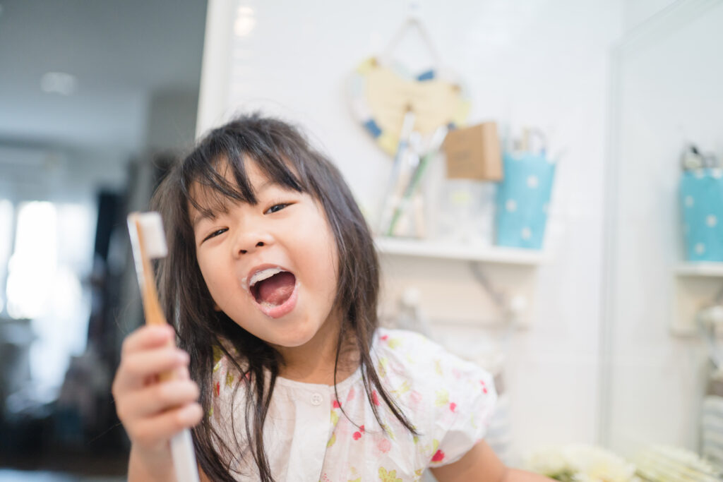 Child smiling with a toothbrush while practicing healthy brushing habits for lifelong oral health.